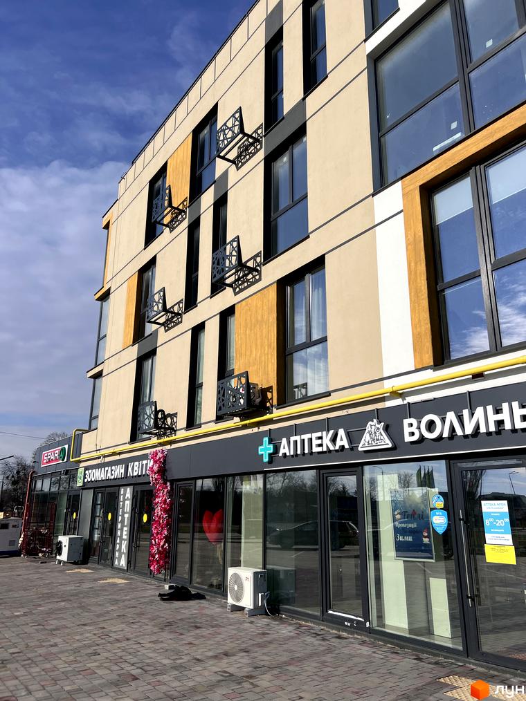 Фасад житлового комплексу U HOME з великими вікнами та декоративними елементами на балконах. На першому поверсі розташовані магазини та аптека.