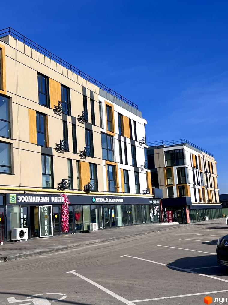 Зовнішній вигляд Новобудови U HOME, що має фасади бежевого, білого та жовтого кольорів. Перед будинком розташована парковка.