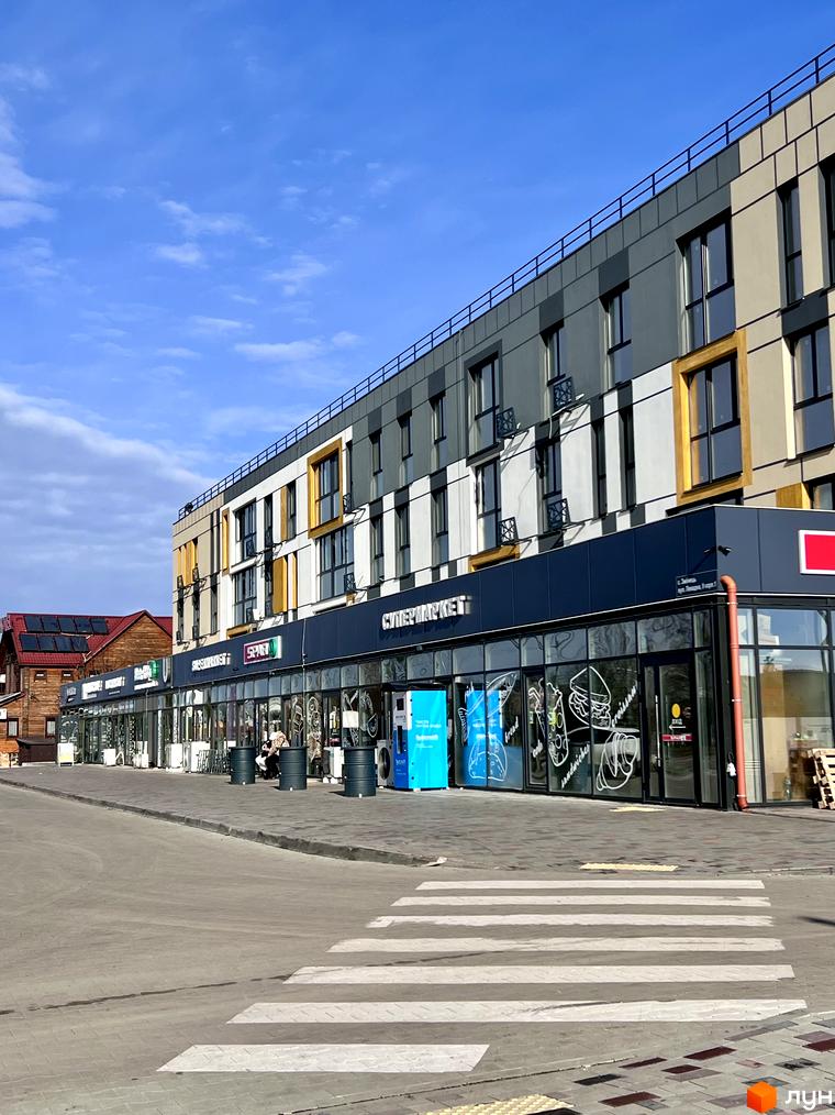 Зовнішній вигляд Житлового комплексу U HOME, фасади з вікнами та магазинами на першому поверсі. На передньому плані пішохідний перехід.