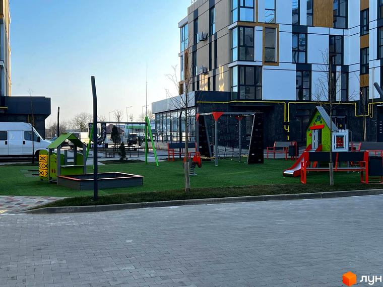 Зображення дитячого майданчика біля будинку в Житловому комплексі U HOME. На території є гірка, пісочниця та гойдалки.