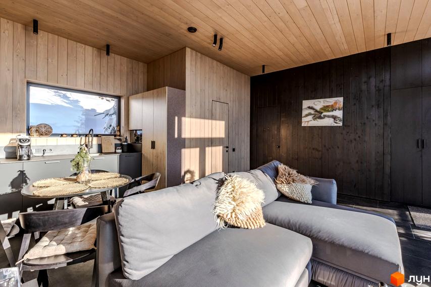 Інтер'єр кухні-вітальні в житловому комплексі КМ Висота 890 з великим вікном та видом на зимовий пейзаж. Сірий диван з декоративними подушками.