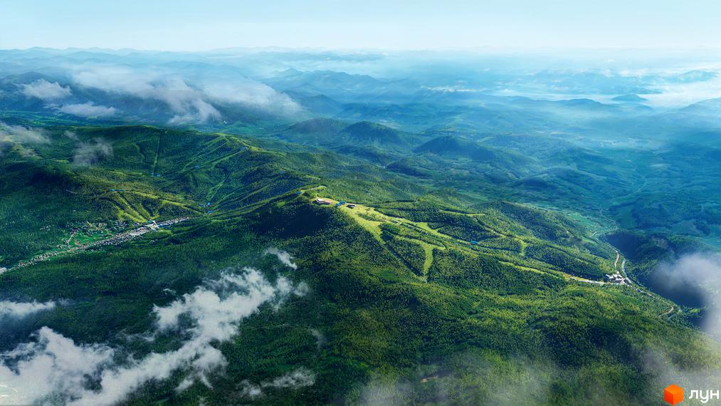 Вид на ONDE Hotel by GORO Mountain Resort з висоти пташиного польоту, що демонструє його розташування серед зелених гір та хмар. Комплекс має сучасну архітектуру та інтегрується в природний ландшафт.