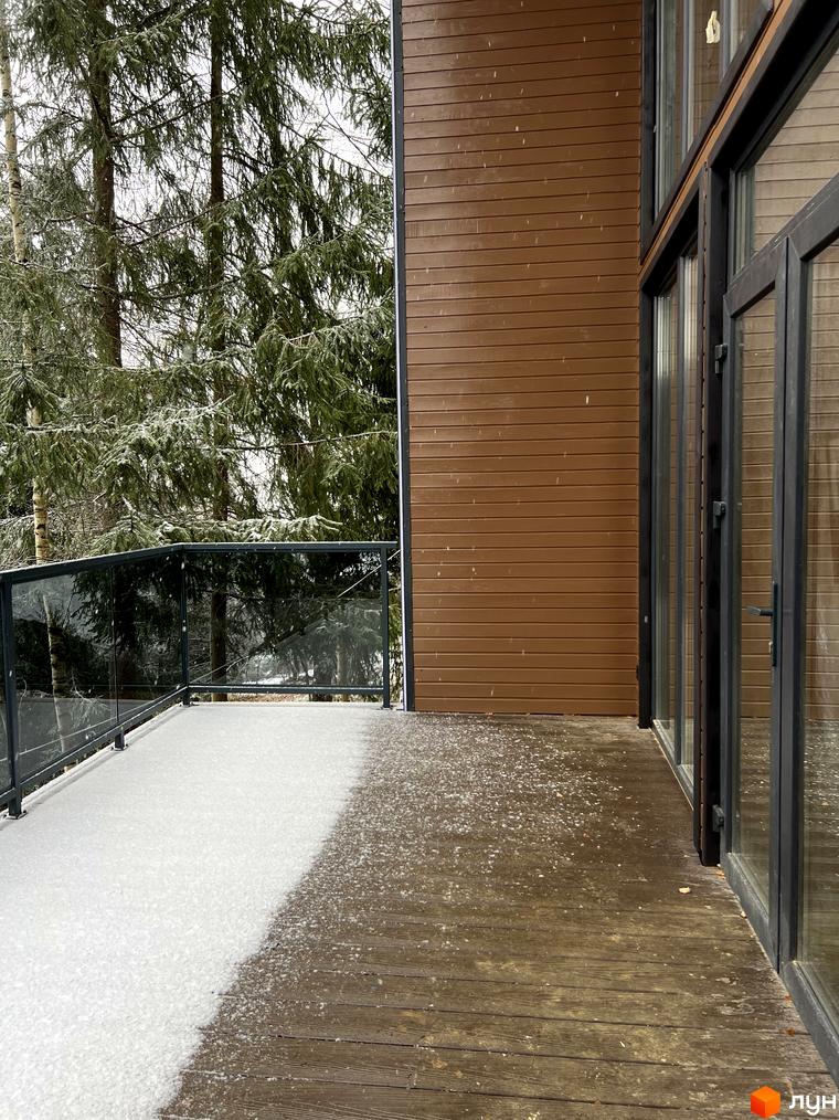 Котеджне містечко GORDO RESIDENCE з коричневою дерев'яною обшивкою та великими вікнами, на терасі лежить сніг. Навколо високі ялини.