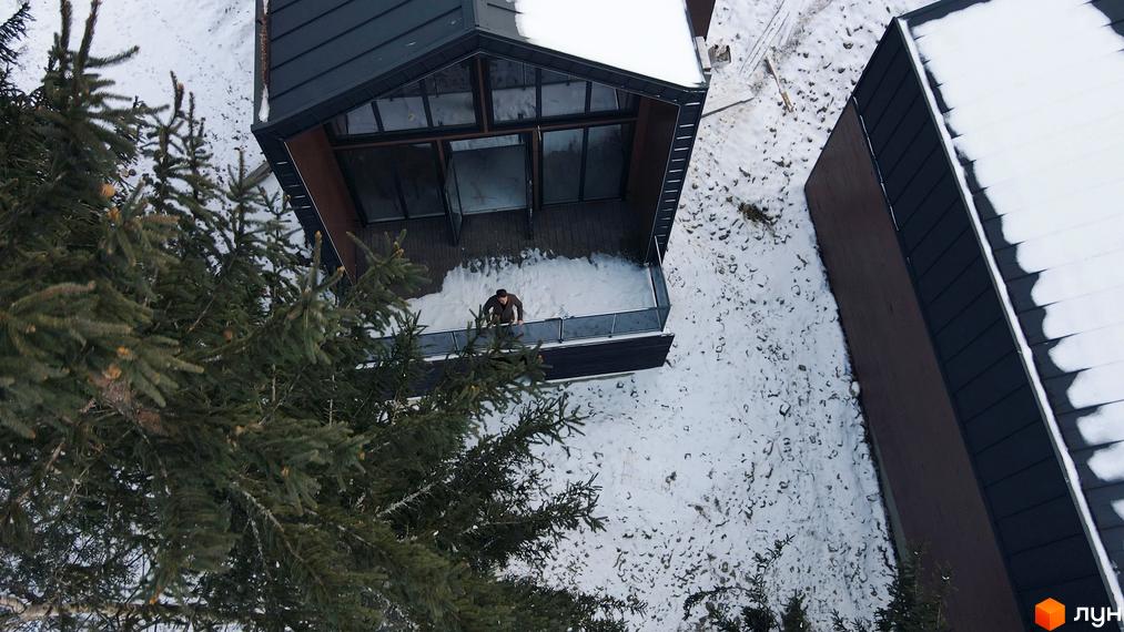 Котеджне містечко КМ GORDO RESIDENCE із темним фасадом та великими вікнами, розташоване серед засніженої території з ялинами.