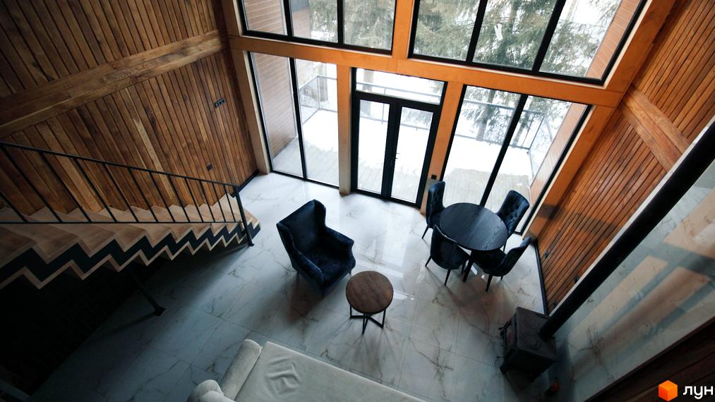 Інтер'єр вітальні в котеджному містечку КМ GORDO RESIDENCE з каміном, обіднім столом та кріслами. Великі вікна з видом на зимовий ліс.