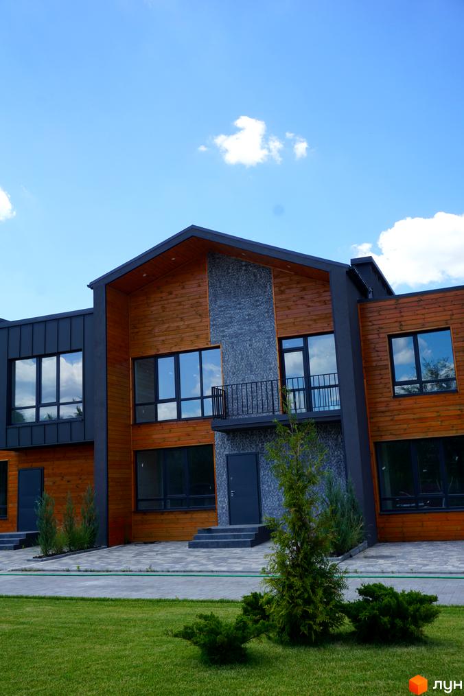 Сучасний котеджний комплекс КМ ЛісоПаркове з дерев'яними фасадами та великими вікнами, зелена доглянута територія перед будинком.