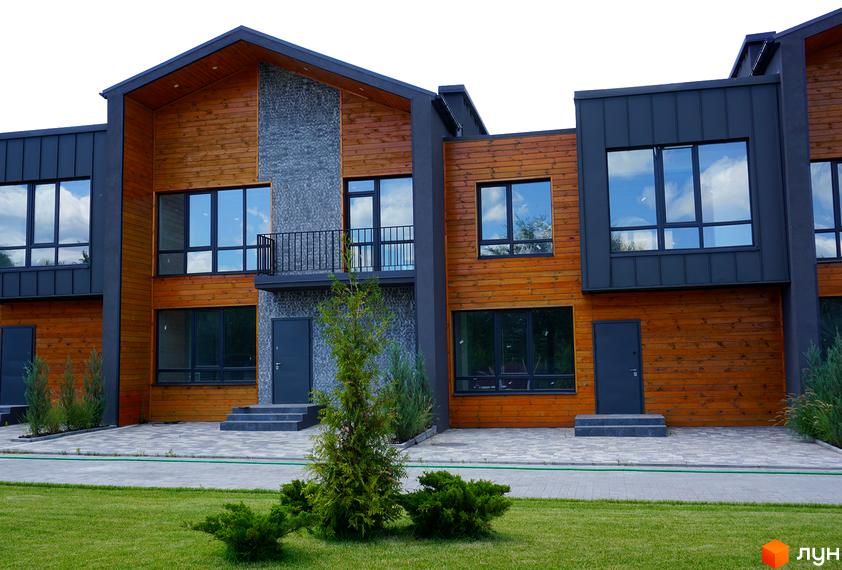 Котеджне містечко КМ ЛісоПаркове. Зовнішній вигляд будинків з дерев'яним фасадом та великими вікнами, прибудинкова територія з доглянутим газоном та зеленими насадженнями.