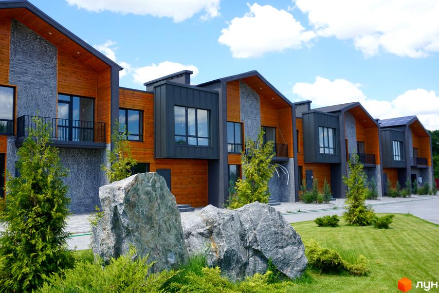 Котеджне містечко КМ ЛісоПаркове. Сучасні будинки з дерев'яним та кам'яним оздобленням, великими вікнами, балконами та доглянутою прибудинковою територією з газоном та деревами.