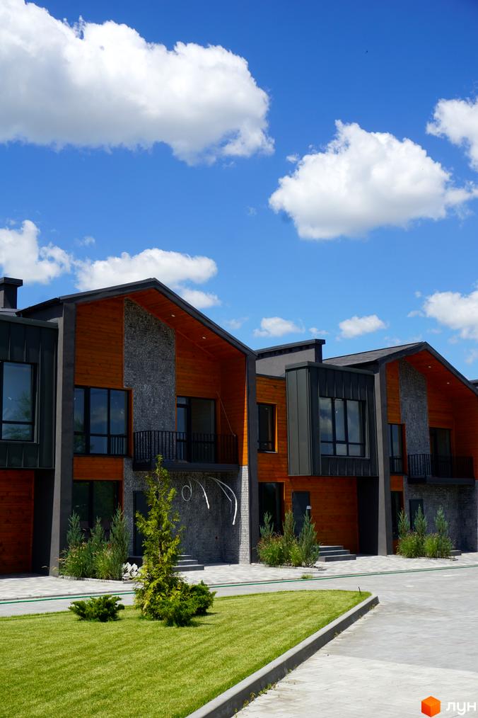 Котеджне містечко КМ ЛісоПаркове. Сучасні будинки з дерев'яними фасадами та сірим каменем, доглянутий газон та зелені насадження.