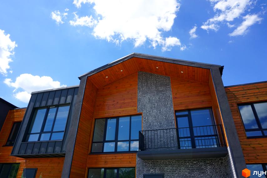 Котеджне містечко КМ ЛісоПаркове. Сучасний житловий комплекс з дерев'яним фасадом та великими вікнами під блакитним небом з хмарами.
