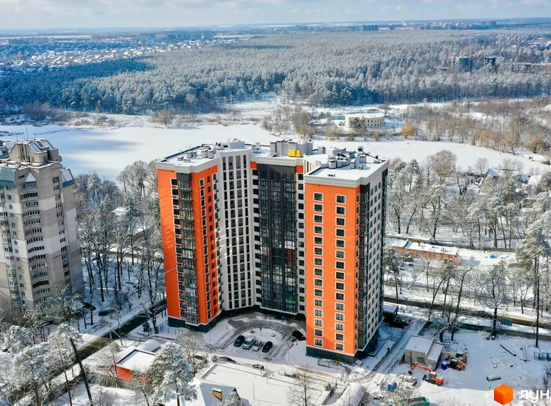 Зовнішній вигляд житлового комплексу Eco Dream з помаранчевими та сірими фасадами взимку. Навколо новобудови розташовані дерева, вкриті снігом, та засніжена територія.