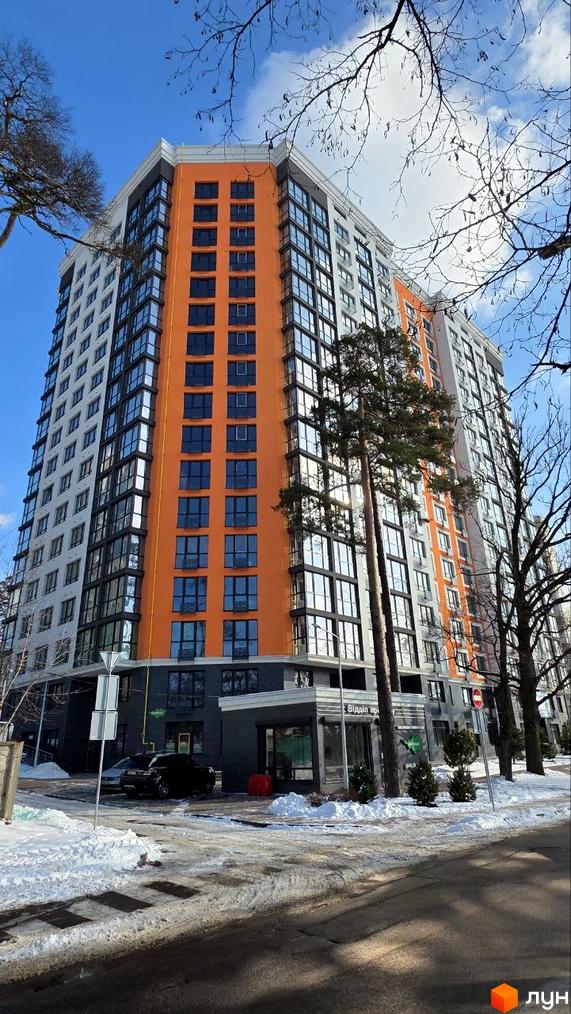 Зовнішній вигляд житлового комплексу Eco Dream з яскравою помаранчевою фасадною частиною та сірими секціями. Навколо комплексу розташована прибудинкова територія з деревами та засніженою дорогою.