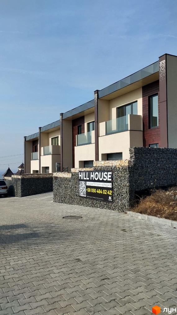Таунхауси HILL HOUSE з кам'яним оздобленням цоколя та сірими дахами на тлі блакитного неба. Прибудинкова територія вимощена плиткою.