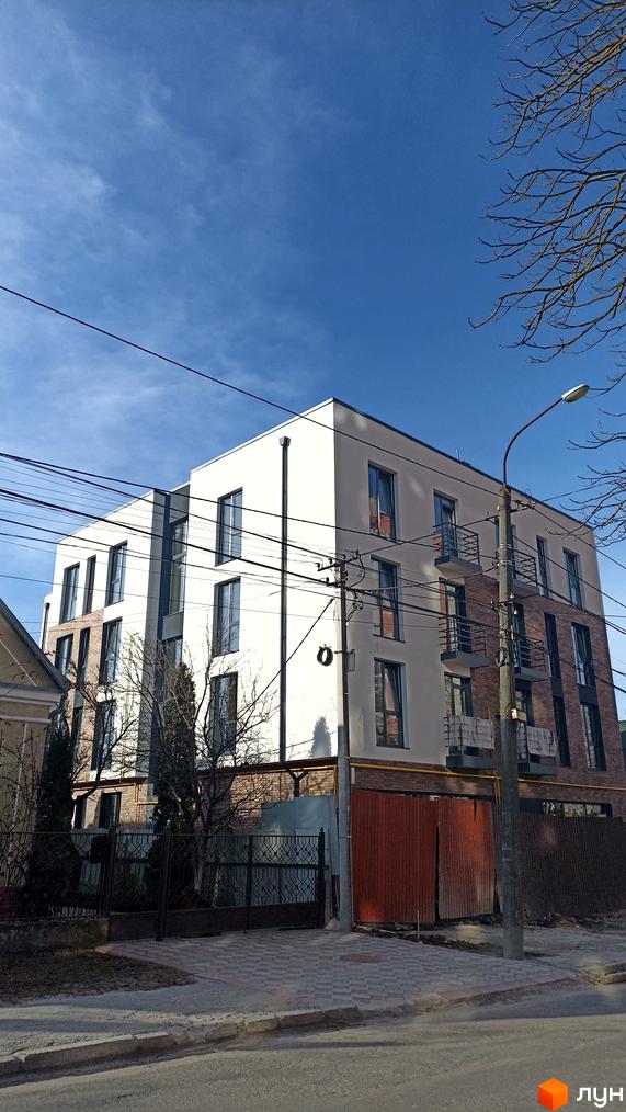 Зовнішній вигляд новобудови на вулиці Омеляна Польового, 3, з цегляними та білими фасадами, балконами та вікнами. Перед будинком розташована огорожа та частина прибудинкової території.