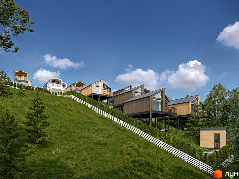 Фото будинків Житлового комплексу VERHGORY на пагорбі. Дерев'яні котеджі з великими вікнами та зеленим газоном.
