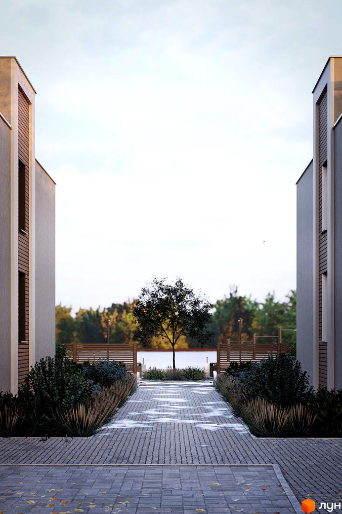 Будинки котеджного містечка The Lake з фасадами світлого кольору та дерев'яними елементами. Дорога з бруківки веде до озера, оточеного зеленню.