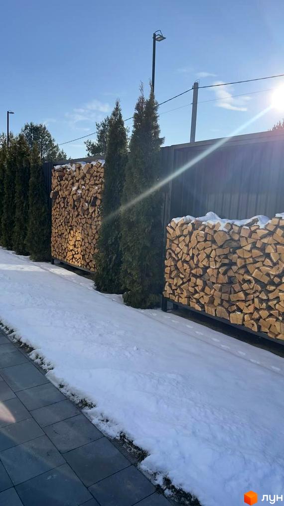 КМ Forest Villa: огороджена територія з акуратно складеними дровами та туями, вкрита снігом. Сучасний ландшафтний дизайн біля новобудови.