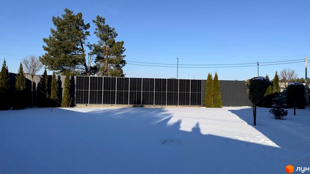 Котеджне містечко КМ Forest Villa з сонячними панелями на паркані та засніженою територією. Навколо ростуть ялини та сосни, створюючи затишну атмосферу.