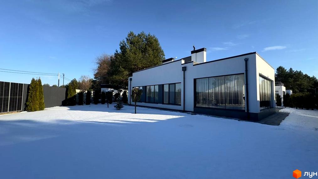 Зовнішній вигляд будинку КМ Forest Villa з великими вікнами та білою фасадною частиною, розташованого на засніженій ділянці з сонячними панелями.