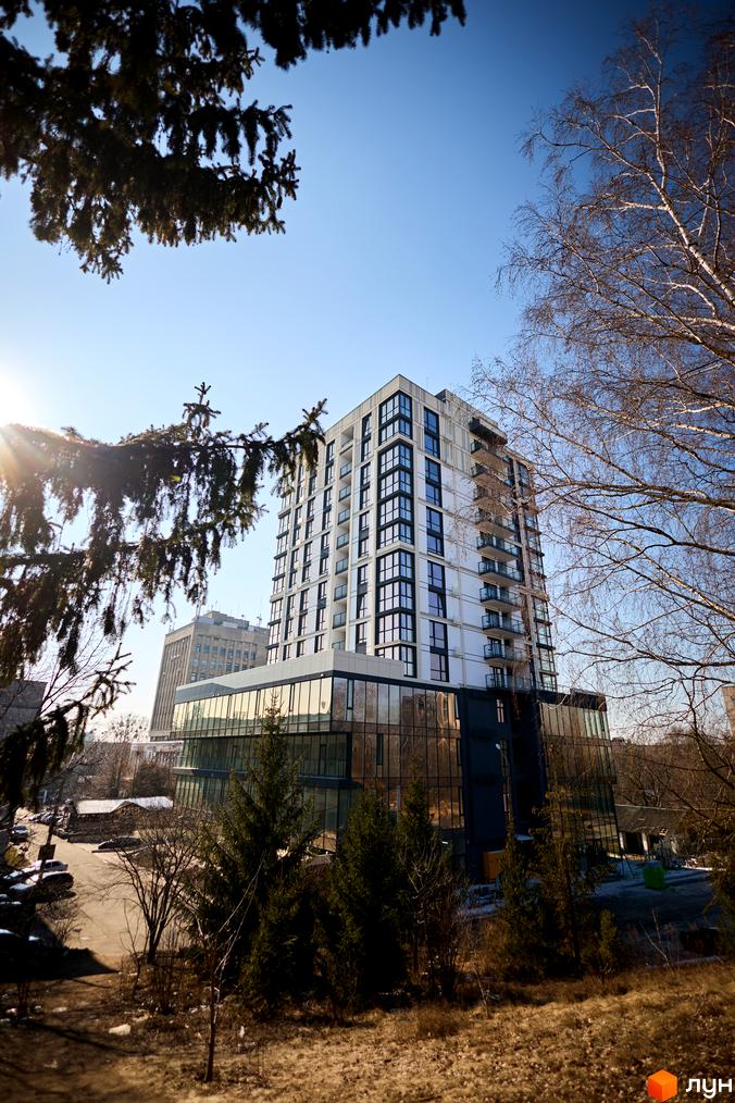 Зображення багатоповерхового будинку в ЖК SOURENZH з великими вікнами та прилеглою зеленою територією.