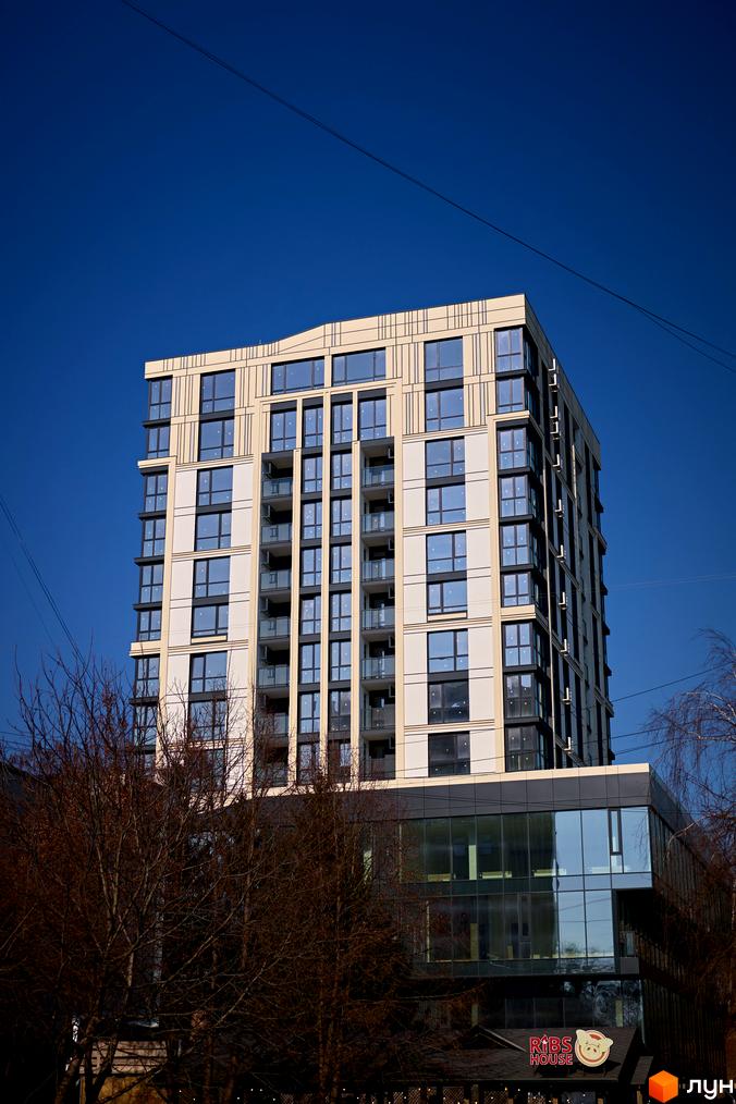 Сучасний житловий комплекс SOOrange з панорамними вікнами та балконами, розташований на фоні ясного блакитного неба. Біля будинку видно дерева та вхідну групу з вивіскою.