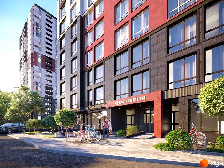 Фасад житлового комплексу Синергія у Києві з червоними та сірими елементами, вікнами та прибудинковою територією з деревами та велосипедами.