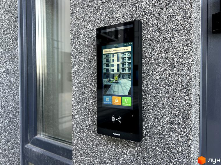 Відеодомофон біля входу в новобудову Park Residence з фасадом з кам'яної крихти. На екрані відображається зображення прибудинкової території з будівельною технікою.