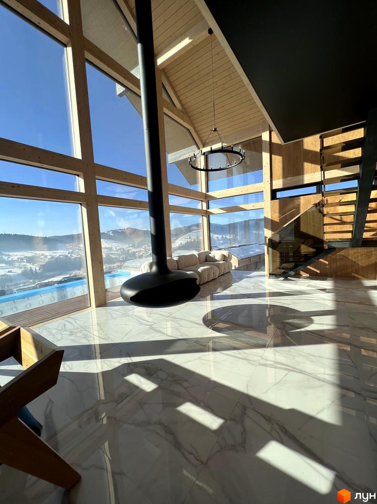 Інтер'єр будинку з панорамними вікнами та каміном у Містечку котеджів Шале Вище Неба з видом на засніжені гори та басейн.