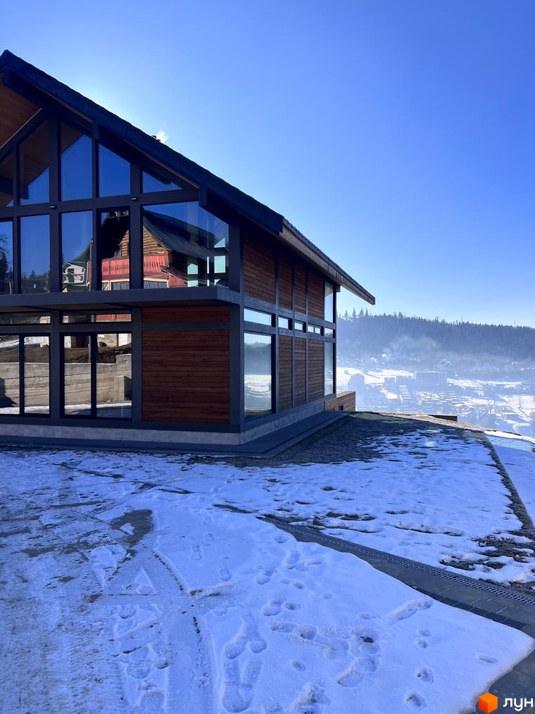 Будинок Котеджного містечка Шале Вище Неба з панорамними вікнами та дерев'яним фасадом. Засніжена територія та зимовий гірський пейзаж.