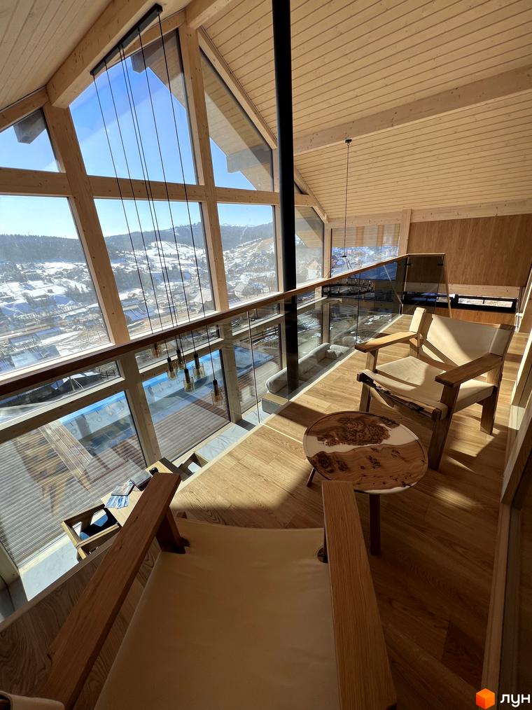 Інтер'єр дерев'яного будинку Котеджного містечка Шале Вище Неба з великими панорамними вікнами. З вікон відкривається краєвид на засніжені гори та селище.