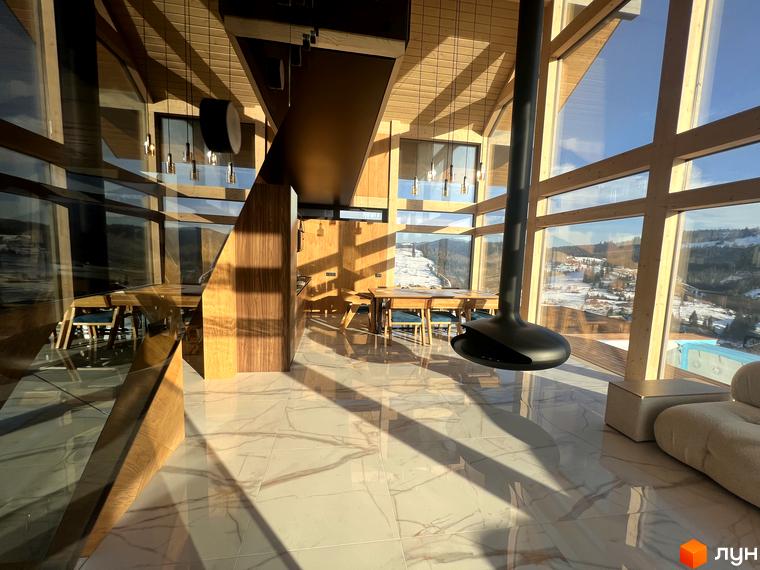 Інтер'єр будинку в Котеджному комплексі Шале Вище Неба з панорамними вікнами та каміном, що висить, з видом на засніжені гори.