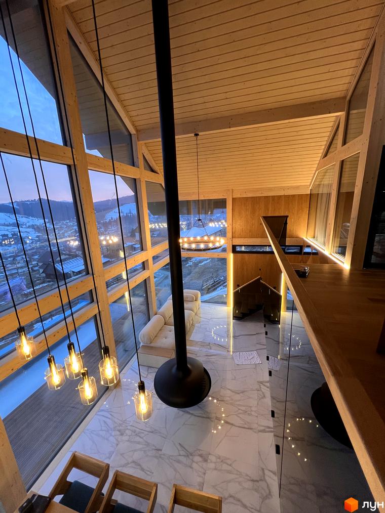 Панорамні вікна Котеджне містечко Шале Вище Неба відкривають вид на засніжені гори. У будинку високі дерев'яні стелі та підвісний камін.