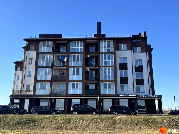 Зовнішній вигляд новобудови ЖК Рать з коричнево-білим фасадом та балконами. На передньому плані припарковані автомобілі.