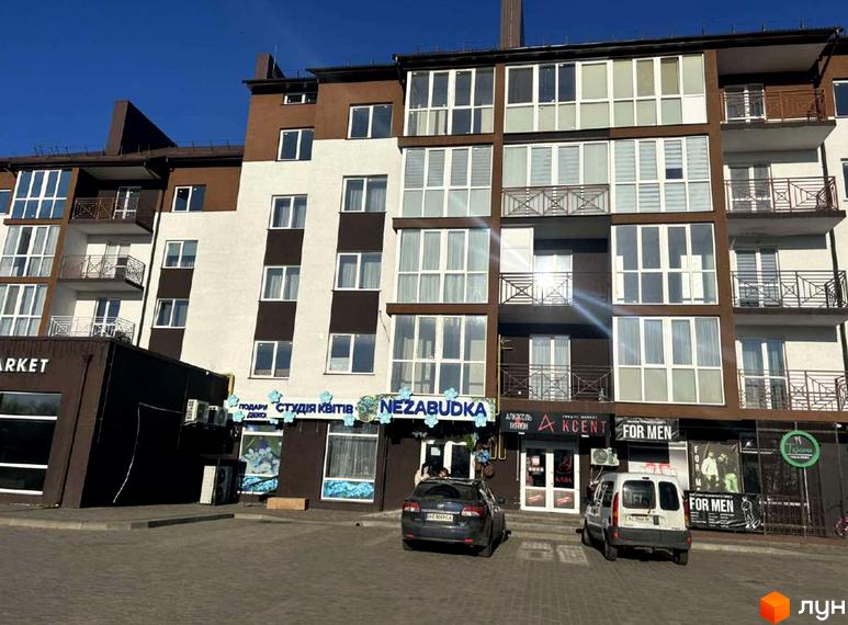 Новобудова ЖК Рать з коричнево-білим фасадом та великими вікнами. Перед будинком розташована парковка з автомобілями.