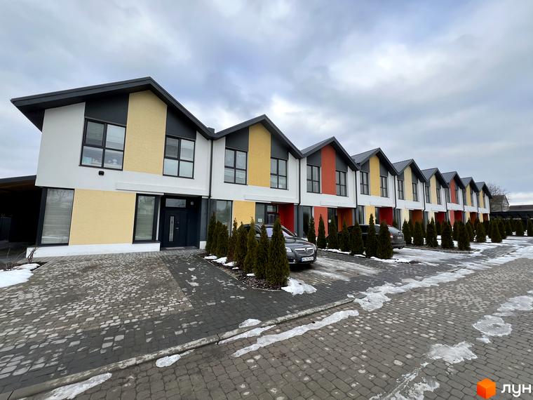 Ряд двоповерхових таунхаусів 9 YARDS з кольоровими фасадами. Перед будинками викладена бруківка, ростуть туї, лежить сніг.