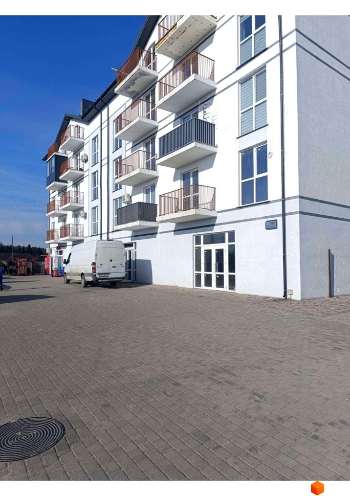 Білий багатоповерховий будинок Житлового комплексу Вижівський з балконами та великими вікнами. Перед ним вимощена бруківкою територія та припаркований білий фургон.