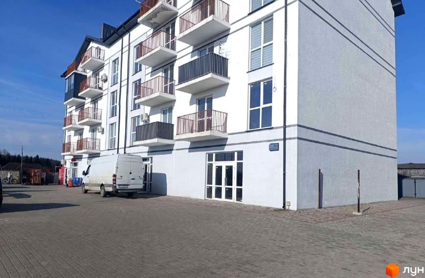 Біла будівля ЖК Вижівський з балконами та скляним входом. На передньому плані бруківка, поруч стоїть білий фургон.