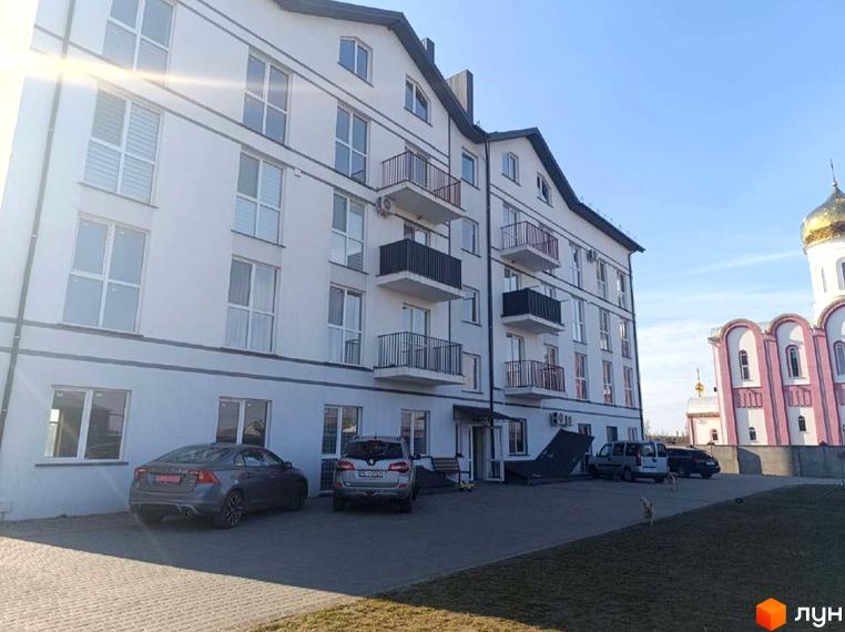 Житловий комплекс Вижівський: білий будинок з темними балконами та дахом. Поруч парковка з авто та церква з золотим куполом.
