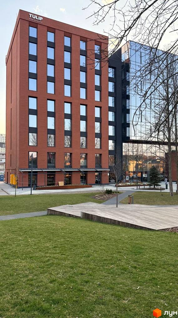Висотна будівля Tulip Residences з великими вікнами та терасами, зелена прибудинкова територія з газоном та дерев'яними настилами.
