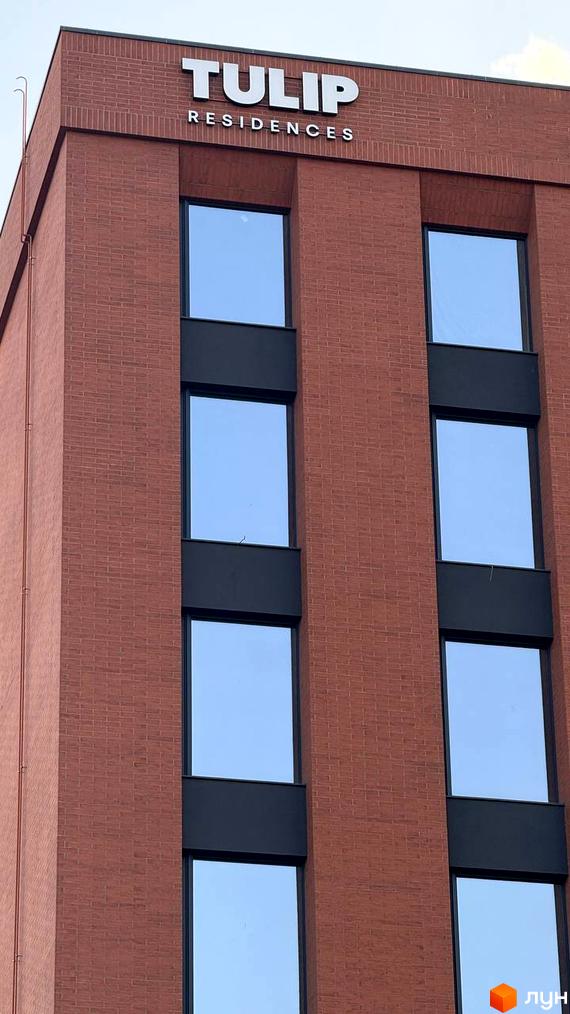 Вид на верхню частину будівлі TULIP RESIDENCES з фасадом з червоної цегли та великими вікнами. На даху видно назву комплексу.