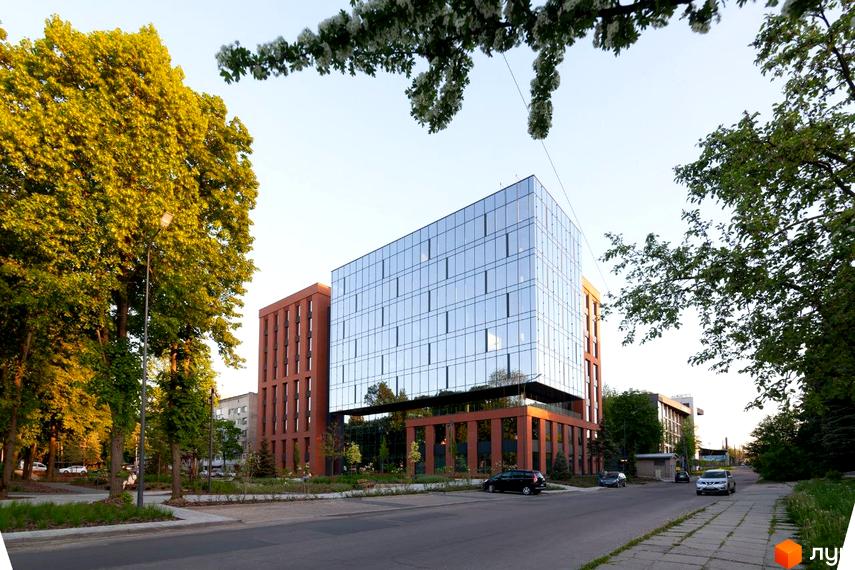 Апарт-комплекс Kristal Plaza з багатоповерховим скляним фасадом та коричневими елементами. Перед будинком розташована дорога та зелені насадження.