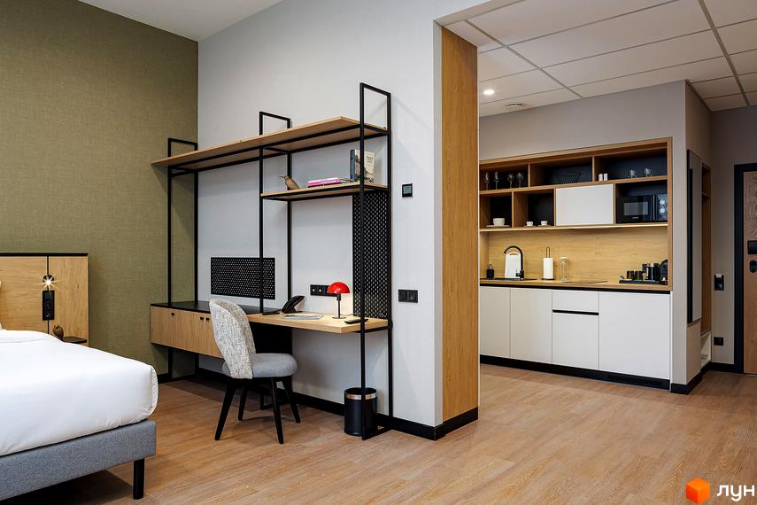 Інтер'єр апартаментів в Kristal Plaza. Простора кімната з робочою зоною та кухнею. Світлі стіни, дерев'яні елементи декору.