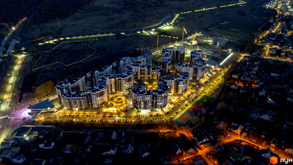Житловий комплекс Синергія Сіті вночі з висоти пташиного польоту. Сучасні багатоквартирні будинки з підсвіченими вікнами та доглянутою прибудинковою територією з парковками та спортивними майданчиками.