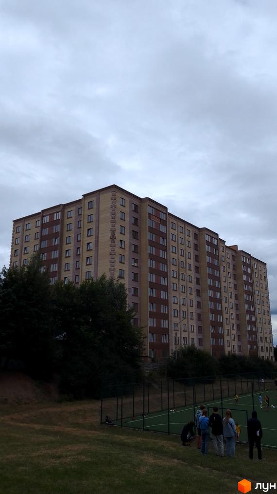 Багатоповерховий житловий комплекс на вулиці Леся Курбаса з цегляним фасадом та вікнами, поруч спортивний майданчик та зелена зона.