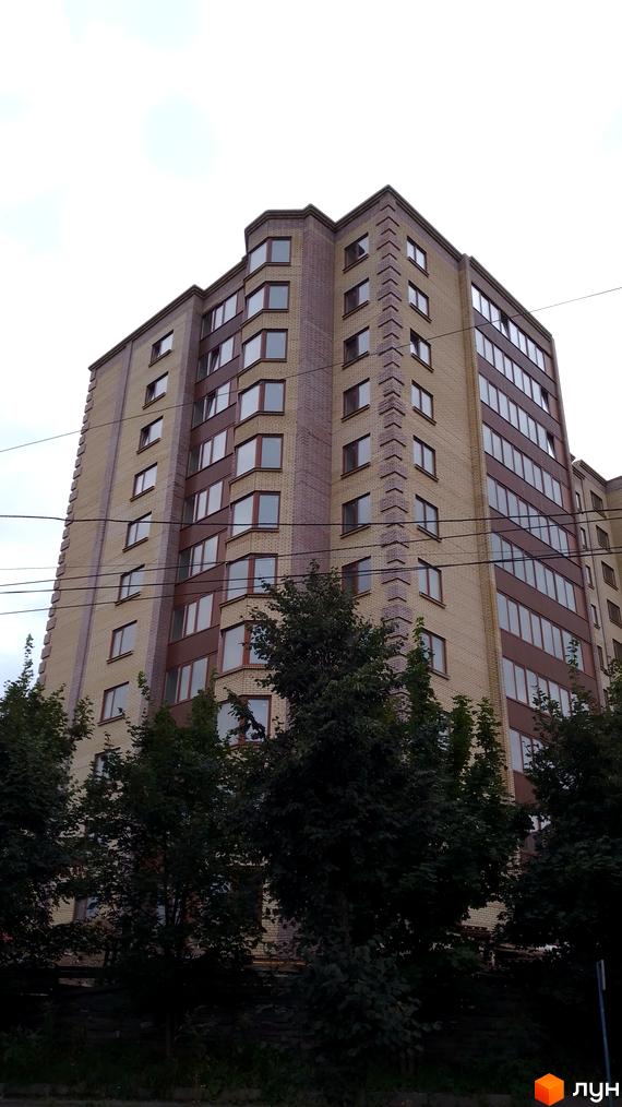 Багатоповерховий житловий комплекс на вулиці Леся Курбаса, з цегляним фасадом світло-бежевого та коричневого кольорів, з великою кількістю вікон. Навколо будівлі ростуть дерева.