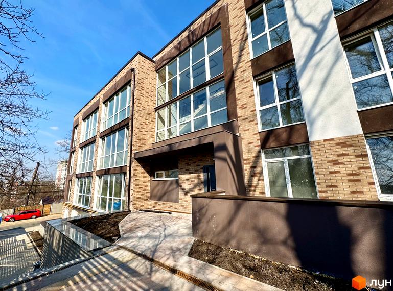 Зовнішній вигляд Клубного будинку Light Residence з великими вікнами та коричневим оздобленням. На передньому плані тротуарна плитка.