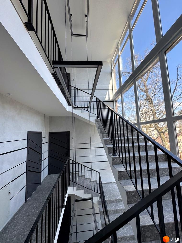 Інтер'єр сходового майданчика в Клубному будинку Light Residence з великими вікнами та чорними поручнями.