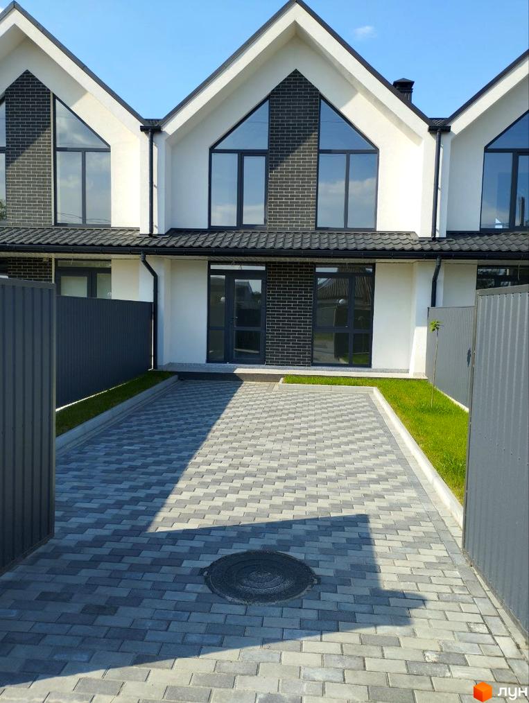 Триповерховий будинок з великими вікнами та бруківкою на подвірʼї. Біля будинку є зелена трава та паркан.