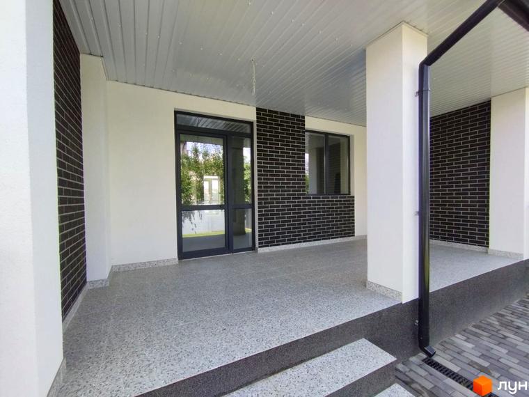 Фасад новобудови на вул. Івана Франка, 14 з білими стінами та темною цеглою. Тераса має світлу плитку та бруківку біля входу.