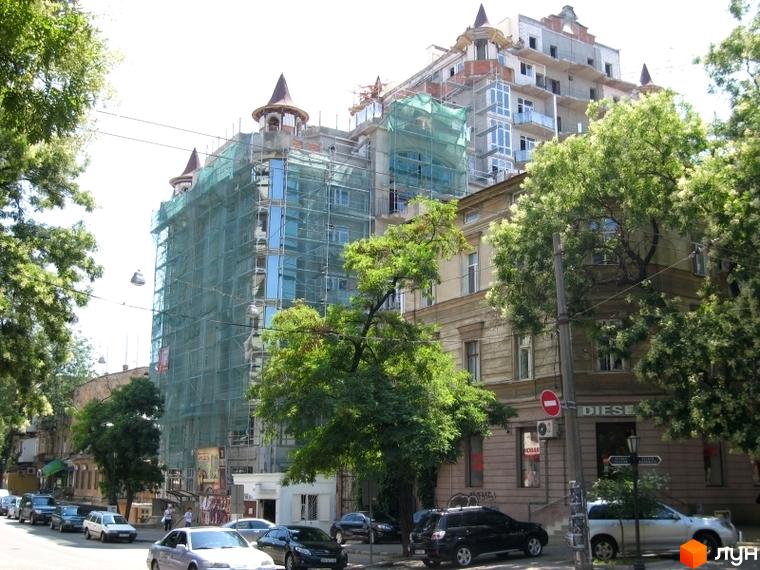 Житловий комплекс Замок цветов, будівля з башточками, обгорнута сіткою, оточена зеленими деревами та автомобілями.